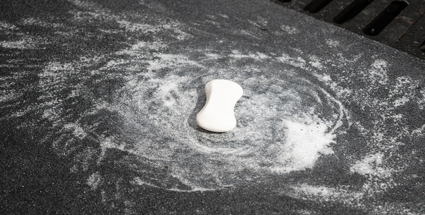 Accessory image for WELKIN Garage Floor Mat (A1204) close-up showing the mat being cleaned with a sponge and soap, emphasizing its durable, easy-to-scrub, and washable cleaning method.