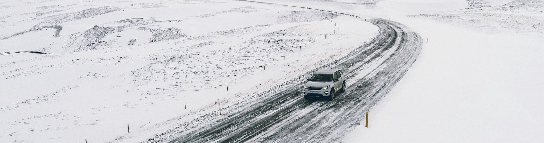 Homepage image showing a white SUV driving on a snowy road with a gray and yellow WELKIN soft roof cargo bag attached to the car top for winter travel and extra storage.