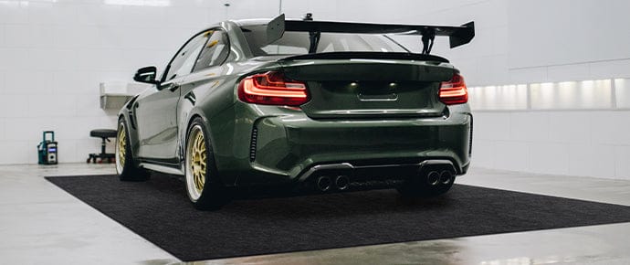Homepage accessory image showing a green sports car parked inside a clean garage or showroom on a large, black WELKIN garage mat for floor protection and vehicle display.