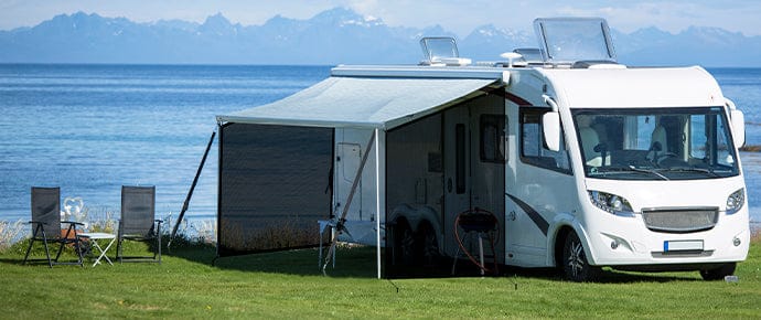 Homepage image showing a large white RV parked by a lake or ocean with snowy mountains in the background, featuring a WELKIN awning sun shade screen attached to the side for sun and privacy protection.
