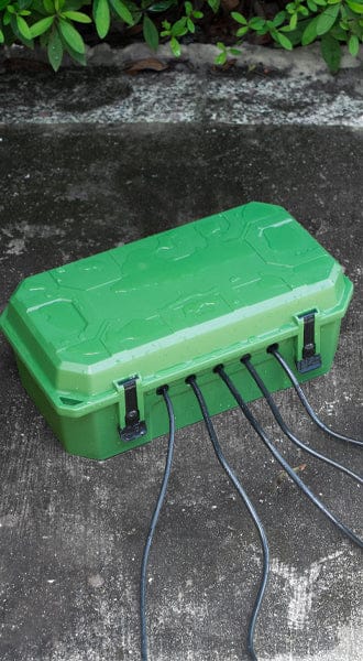 Homepage image showing a green outdoor waterproof cable connection box (power cord protector) on a concrete surface, with multiple black power cords securely running out of the side ports for safety and weather protection.